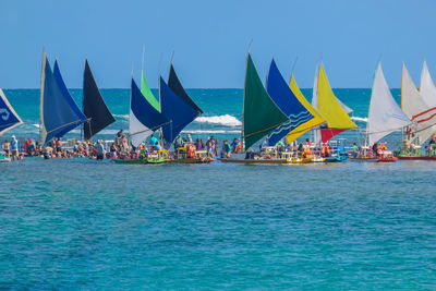 People on colorful sailboats in sea against clear blue sky