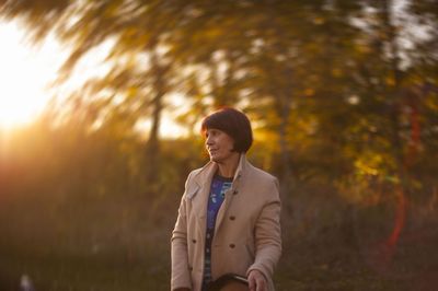 Smiling woman looking away while standing on land against trees