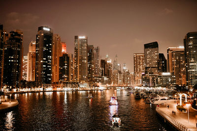 Illuminated buildings by river against sky in city at night