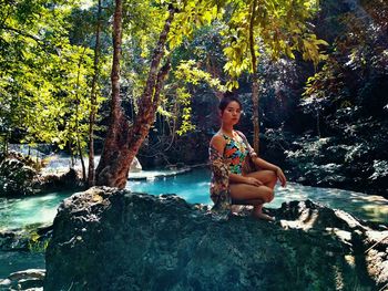 Portrait of young woman sitting on rock in forest