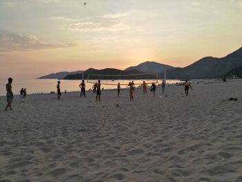 People playing at beach against sky during sunset