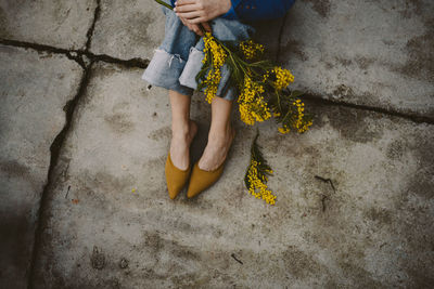 Low section of woman sitting on the floor with yellow flower