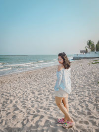 Young woman standing at beach against clear sky
