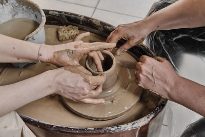 Hands of senior woman and girl sculpting clay vase on potter's wheel at pottery training lesson.