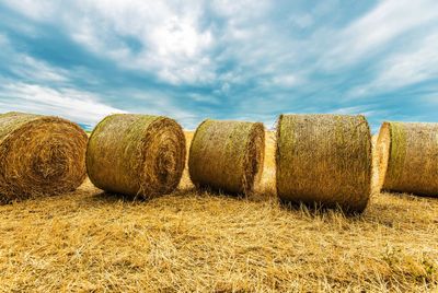 Hay bales on agricultural field against cloudy sky