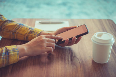 Midsection of man holding smart phone on table