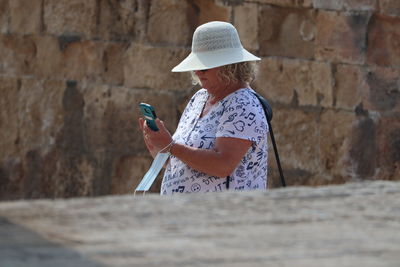 Woman holding umbrella while standing against wall