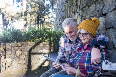 Smiling couple reading newspaper while sitting on bench outdoors