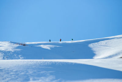 People skiing on snowcapped mountain against blue sky