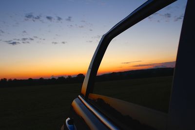 Close-up of side-view mirror against sunset sky