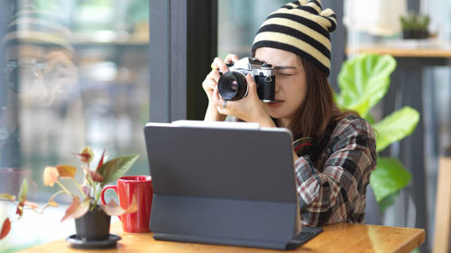 Young woman photographing by digital tablet while sitting on table