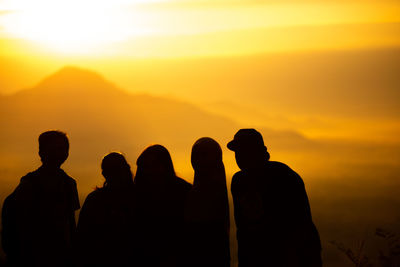 Silhouette people standing against mountains and orange sky during sunset