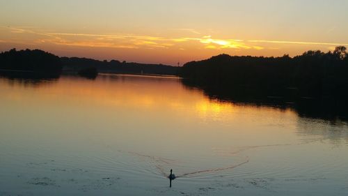 Silhouette person by lake against sky during sunset