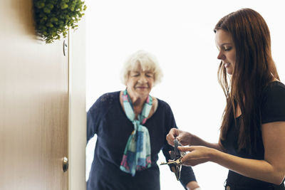 Elderly woman looking at granddaughter unlocking front door of house