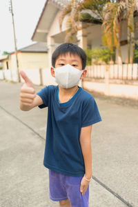 Full length portrait of boy standing showing thumbs up while standing on road