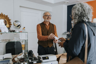 Male antique shop owner giving bill to female customer at counter in store