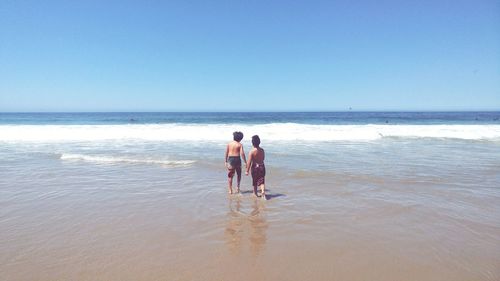 Friends wading in sea against clear sky