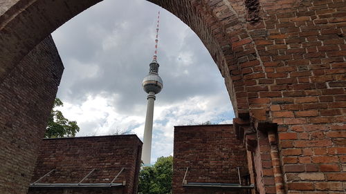 Low angle view of fernsehturm seen through arch against cloudy sky