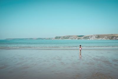 Rear view of girl running at beach against clear blue sky during sunny day