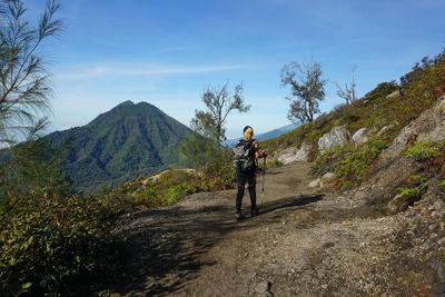 Rear view of woman standing on dirt road against sky