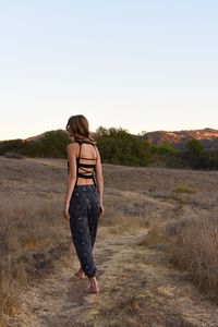 Rear view of woman standing on field against clear sky