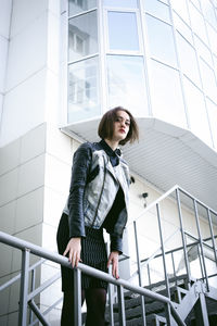 Portrait of young woman leaning on railing against building