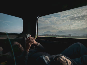 Young man using smart phone while lying in car