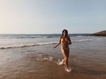 Full length portrait of young woman standing on beach against clear sky