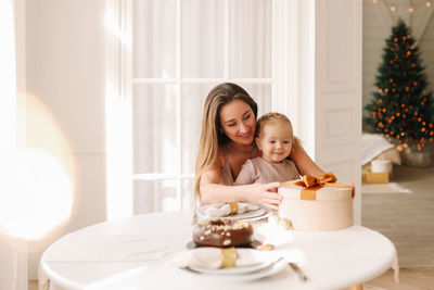 Happy mom and child are sitting at the dining table eating a christmas cupcake on holiday at home