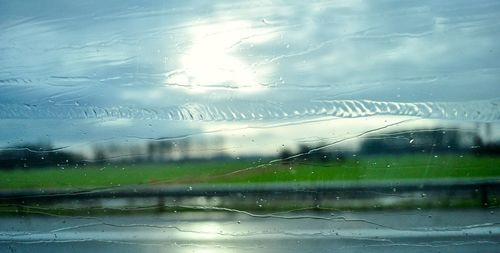 Close-up of wet glass against sky during rainy season