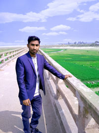 Portrait of young man standing on field against sky