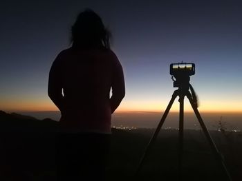 Rear view of silhouette photographing against sky during sunset