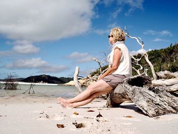 Woman sitting on beach against sky