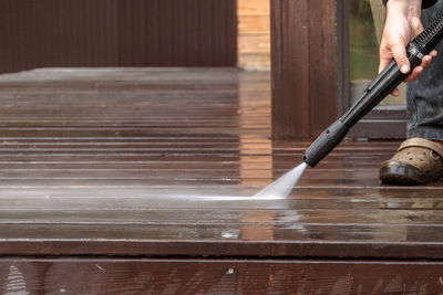 Man cleaning walls and floor with high pressure power washer. washing terrace wood planks and cladd