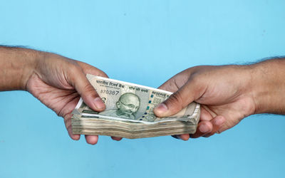 Cropped hands of person holding paper currency against blue background