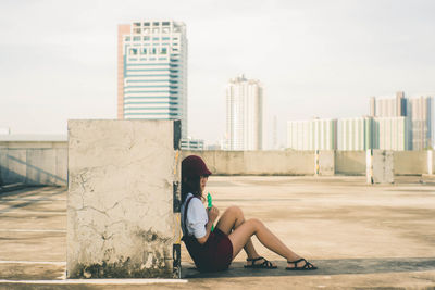 Full length of woman sitting against modern buildings in city