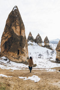 Rear view of person on rock against sky during winter