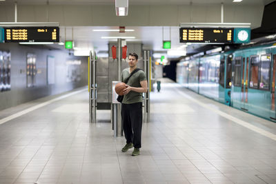 Portrait of young man with basketball walking at railroad station platform