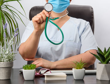 Midsection of doctor wearing mask holding stethoscope at clinic