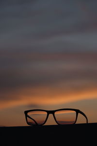 Close-up of silhouette eyeglasses against orange sky