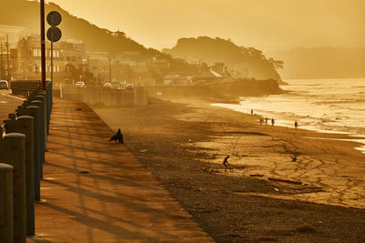 Scenic view of beach with silhouette people against orange sky during sunrise