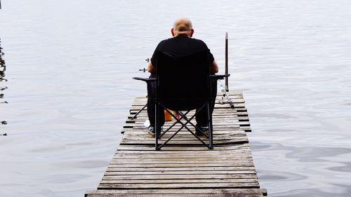 Rear view of bald man sitting on pier over lake