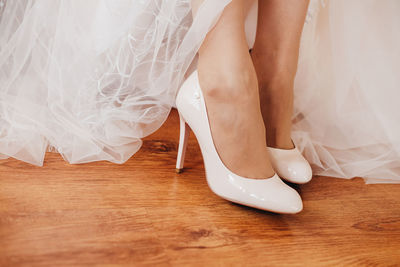 Low section of bride wearing stiletto while standing on hardwood floor