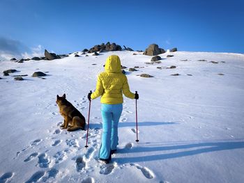 Rear view of woman with hooded winter jacket hiking in the mountains together with her dog 