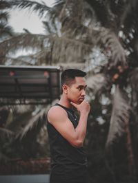 Young man looking away while standing on tree