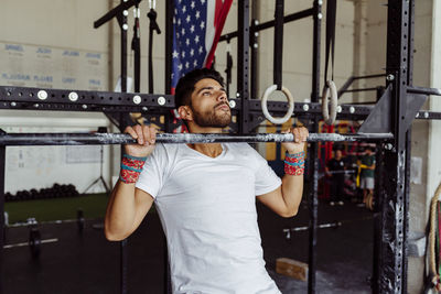 Young athlete doing chin-ups on rod at gym