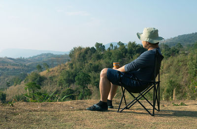Rear view of man sitting on chair against mountain