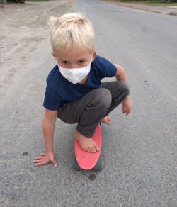 High angle view of cute boy on street skateboarding and wearing a mask