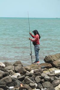 Man fishing in sea against sky