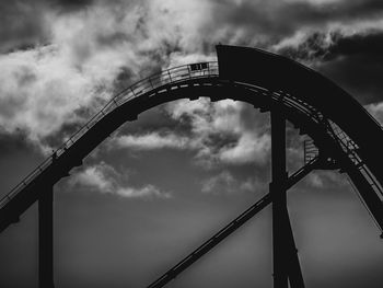 Low angle view of silhouette amusement park against cloudy sky